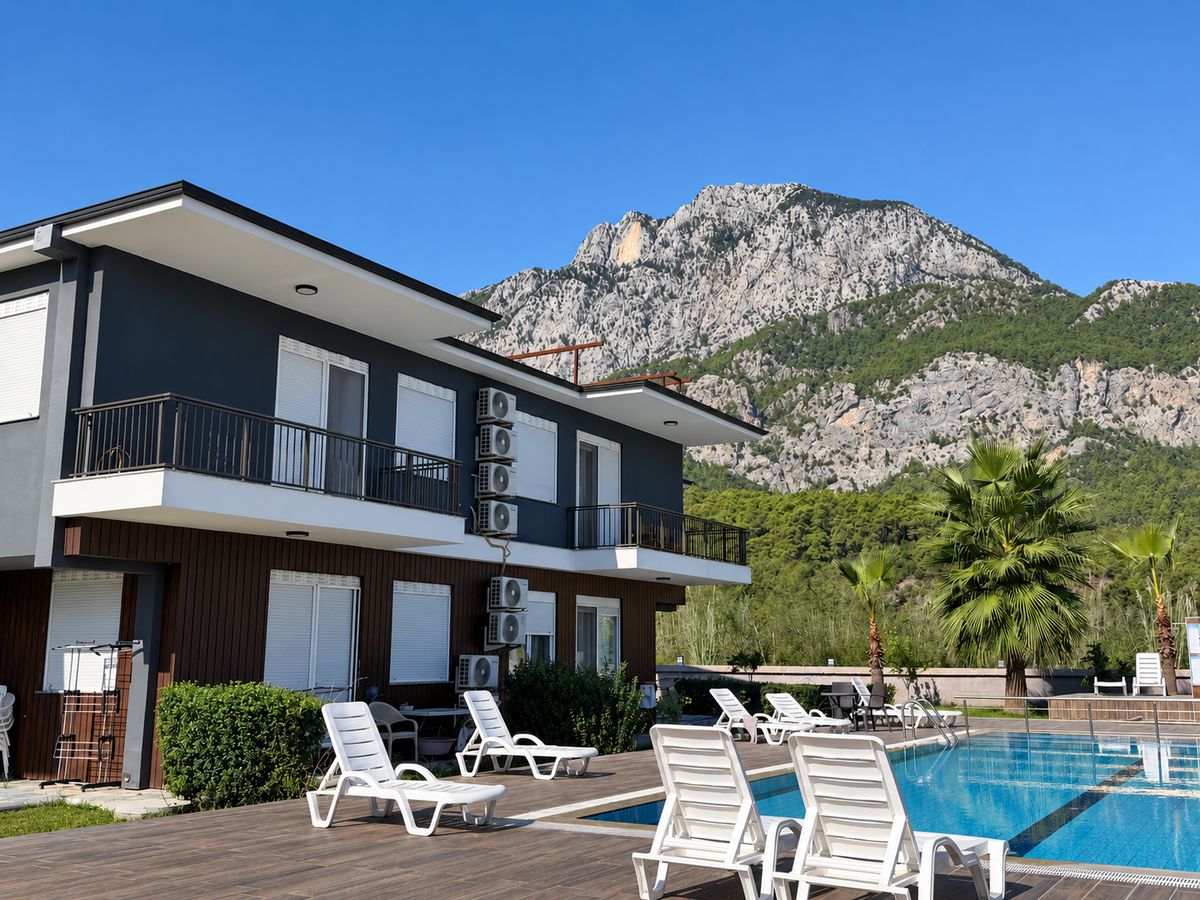 Two-storey apartment building with balconies, sun loungers and a mountain behind