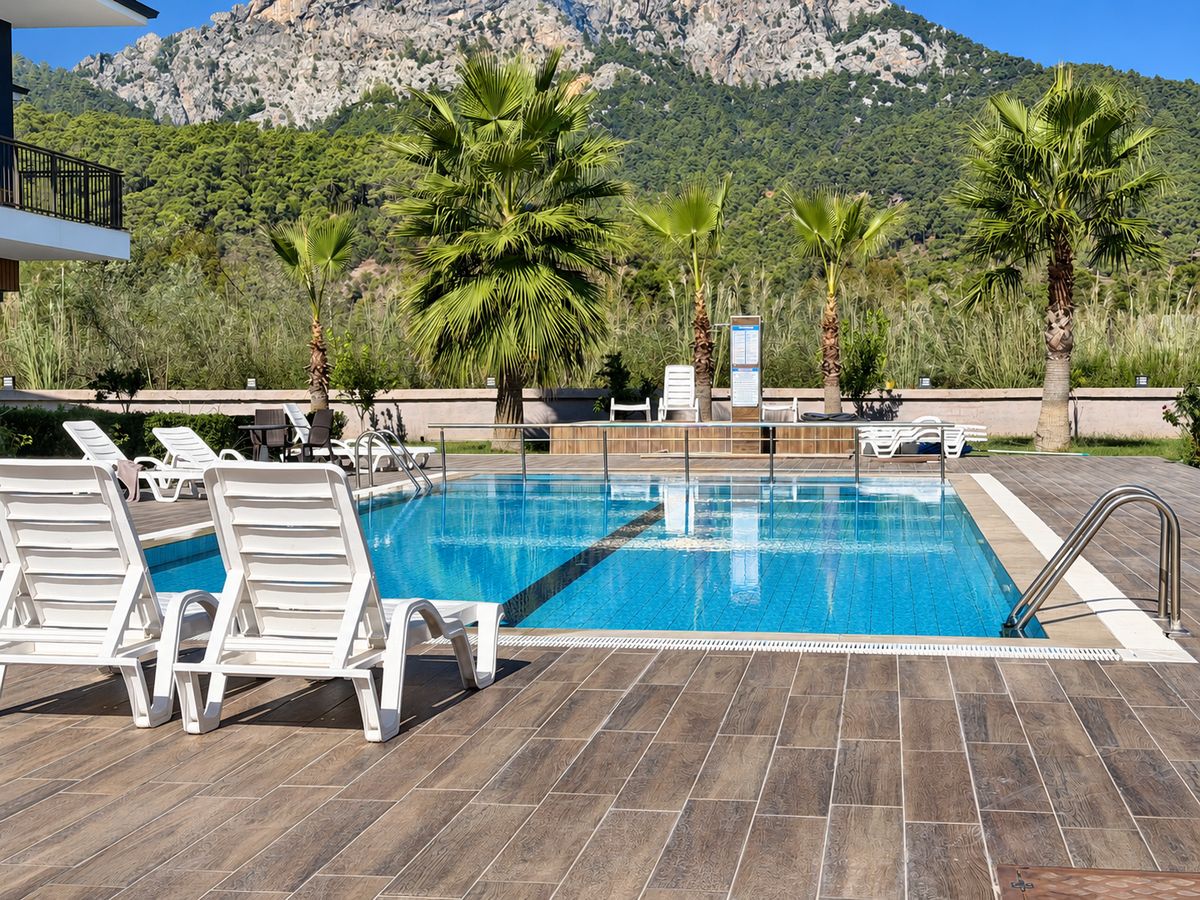 White sun loungers beside the pool with palms and a mountain view